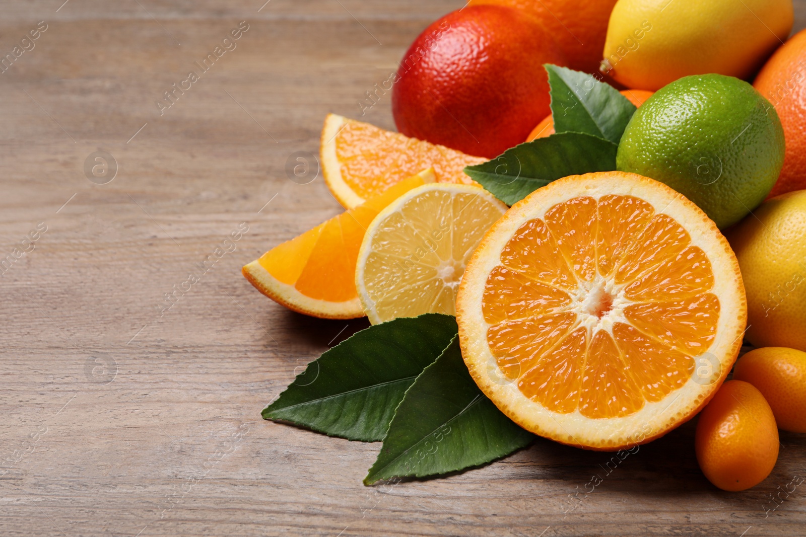 Photo of Fresh juicy citrus fruits with green leaves on wooden table. Space for text