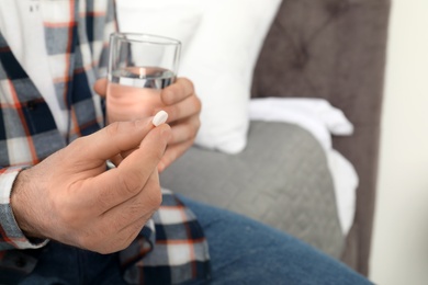 Photo of Man with pill and glass of water indoors, closeup