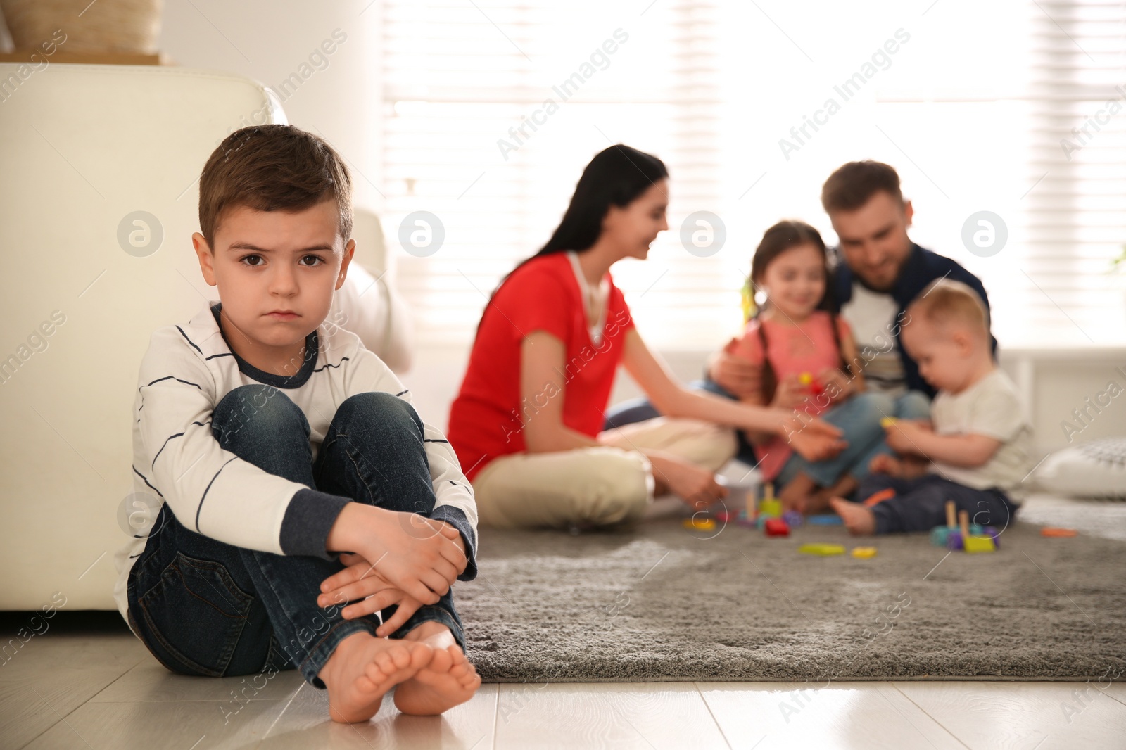 Photo of Unhappy little boy feeling jealous while parents spending time with other children at home