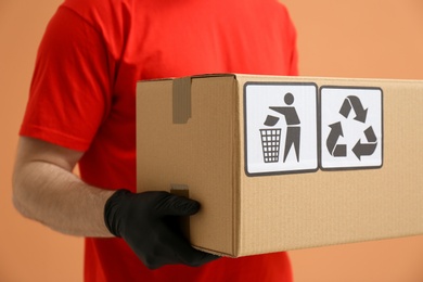 Courier holding cardboard box with different packaging symbols on orange background, closeup. Parcel delivery