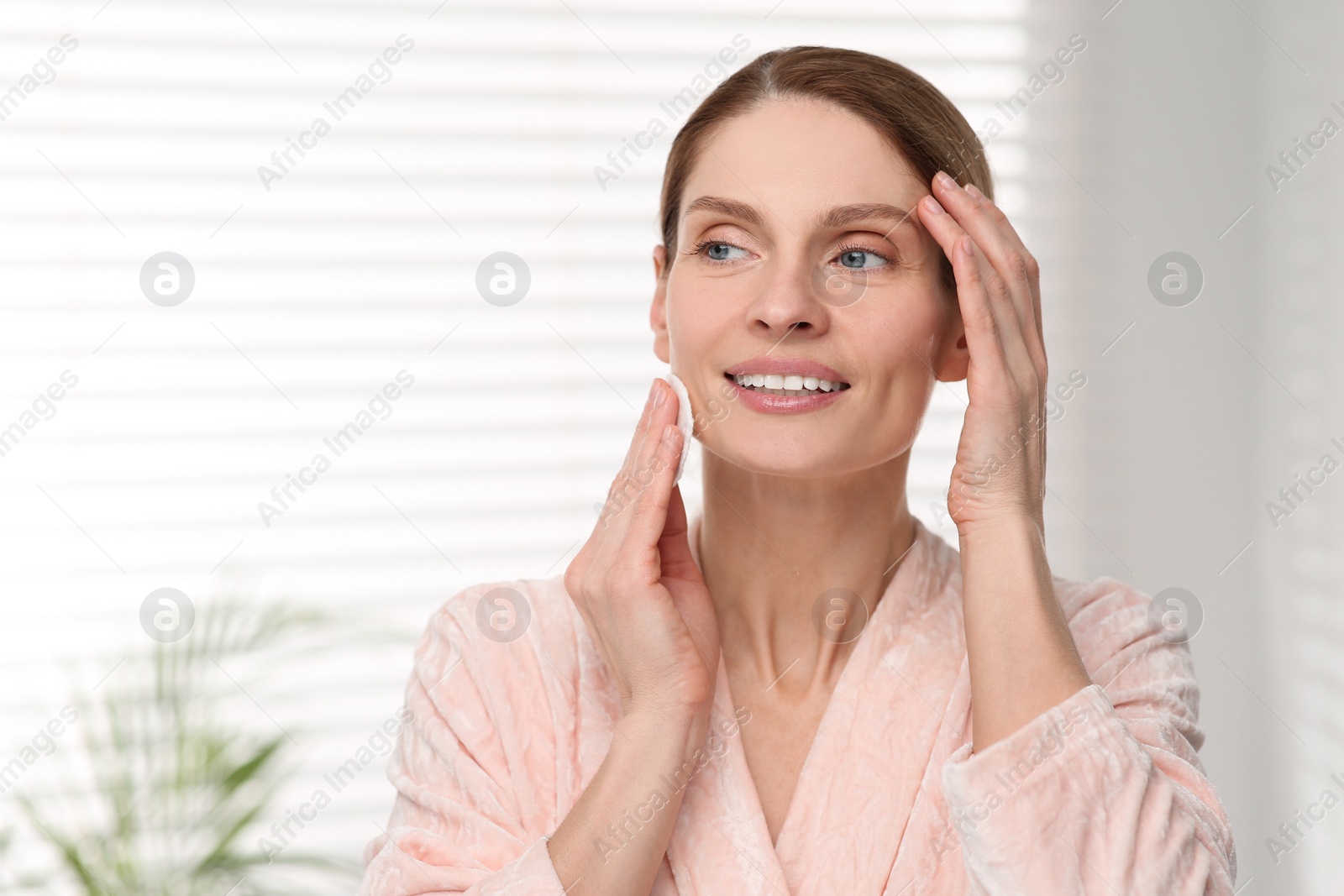 Photo of Beautiful woman removing makeup with cotton pad indoors