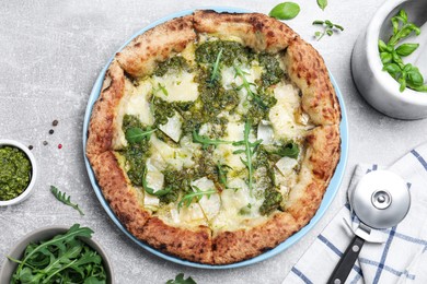 Photo of Delicious pizza with pesto, cheese and arugula served on grey table, flat lay