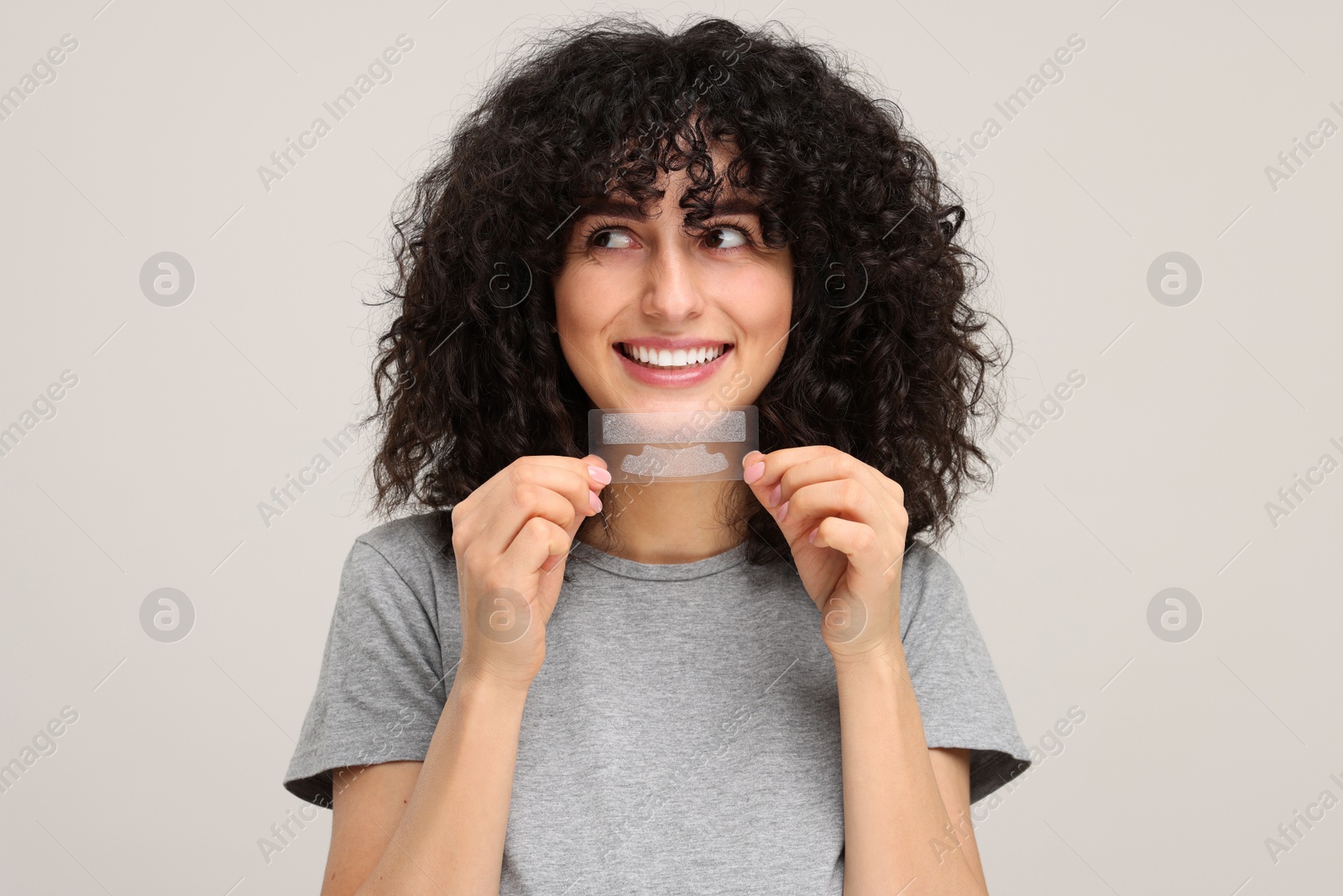 Photo of Young woman holding teeth whitening strips on light grey background