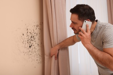 Image of Mold removal service. Man talking on phone and looking at affected wall in room