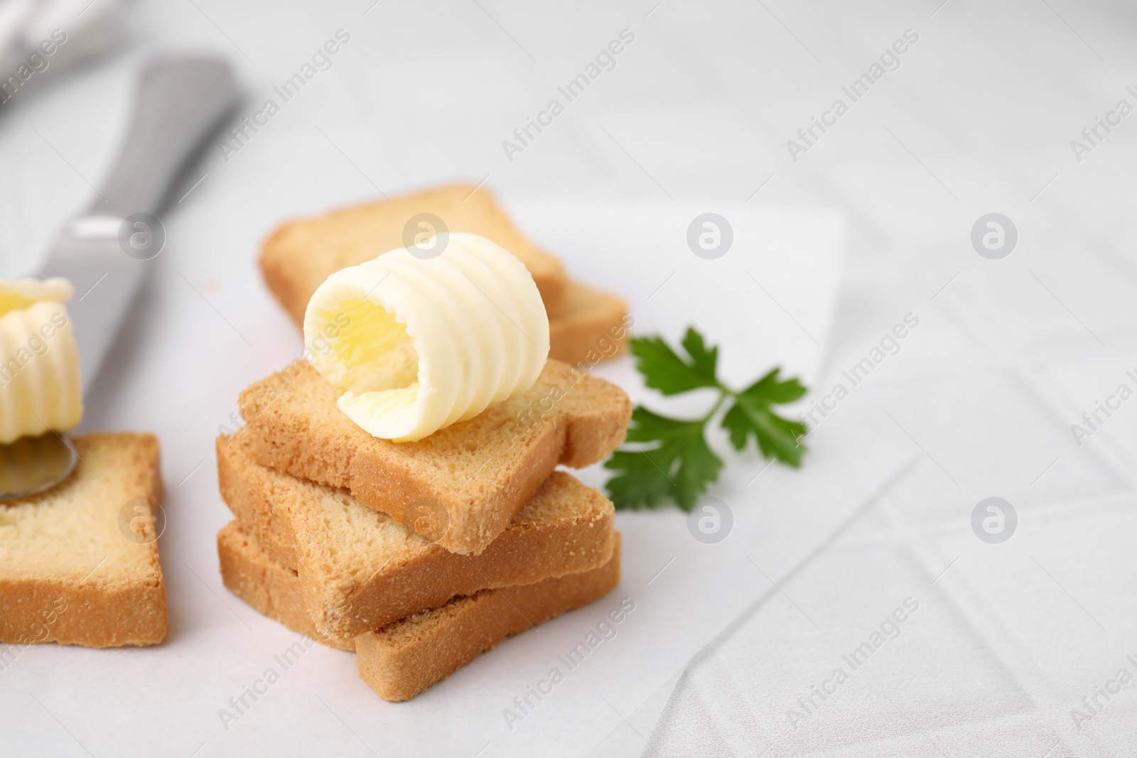Photo of Tasty butter curls, knife and pieces of dry bread on white tiled table, closeup. Space for text