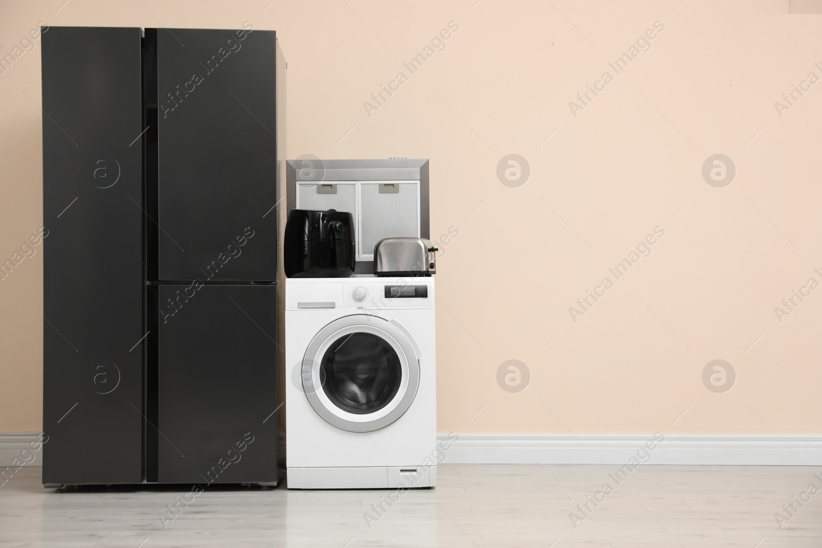 Photo of Modern refrigerator and other household appliances near beige wall indoors, space for text