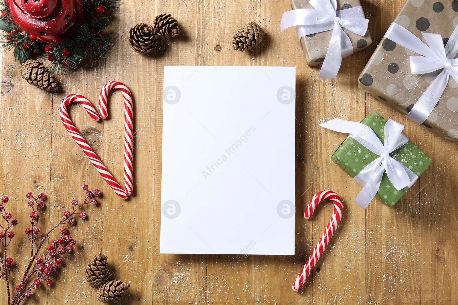 Photo of Flat lay composition with blank paper sheet, candy canes and Christmas decor on wooden table, space for text. Letter to Santa