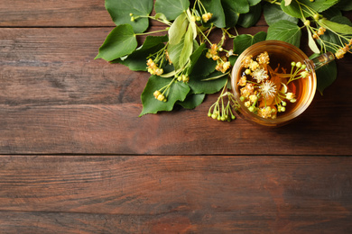 Cup of tea and linden blossom on wooden table, flat lay. Space for text