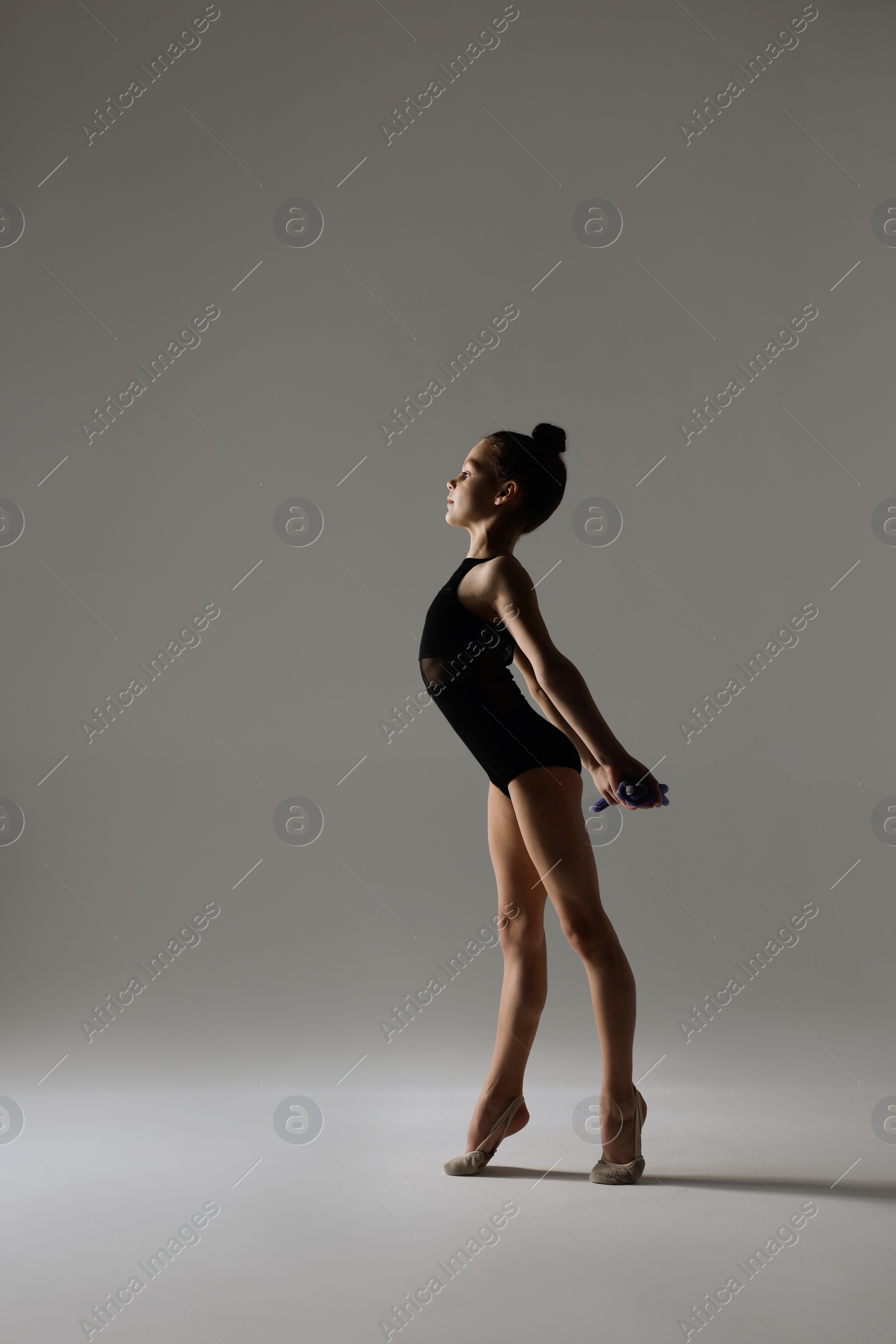 Photo of Cute little girl doing gymnastic exercise with rope on white background