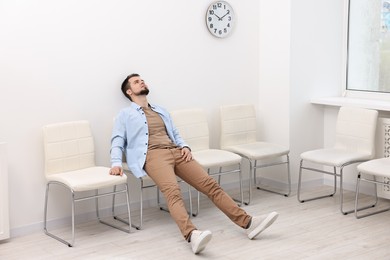 Photo of Tired man sitting on chair and waiting for appointment indoors