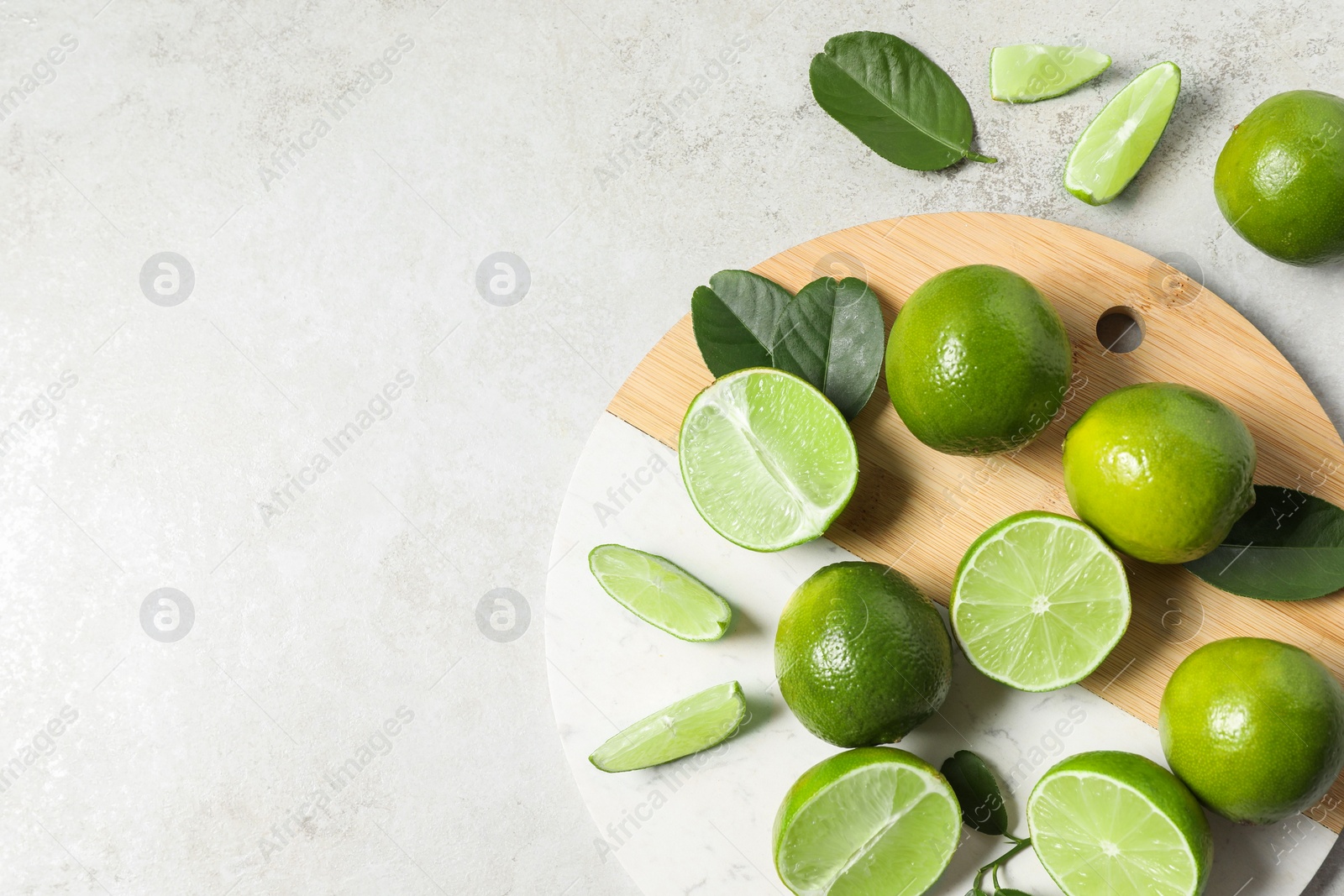 Photo of Fresh ripe limes and leaves on light table, top view. Space for text