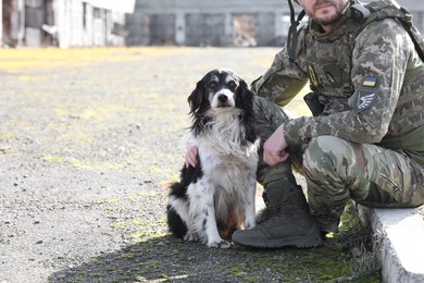 Photo of Ukrainian soldier with stray dog outdoors on sunny day, closeup. Space for text
