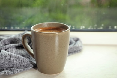 Photo of Cup of hot drink on window sill against glass with rain drops, space for text