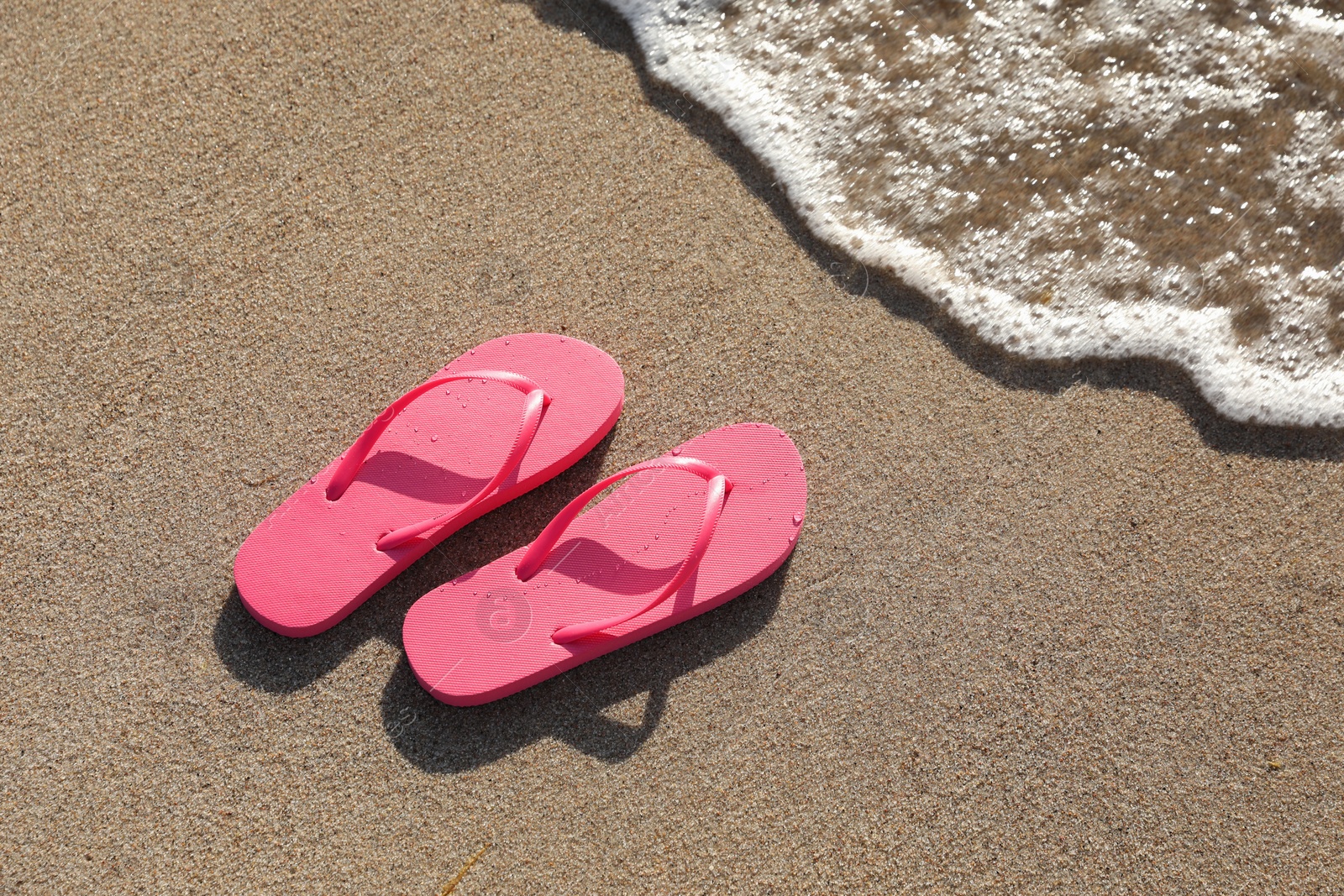 Photo of Stylish bright pink flip flops on sand near sea, above view. Space for text