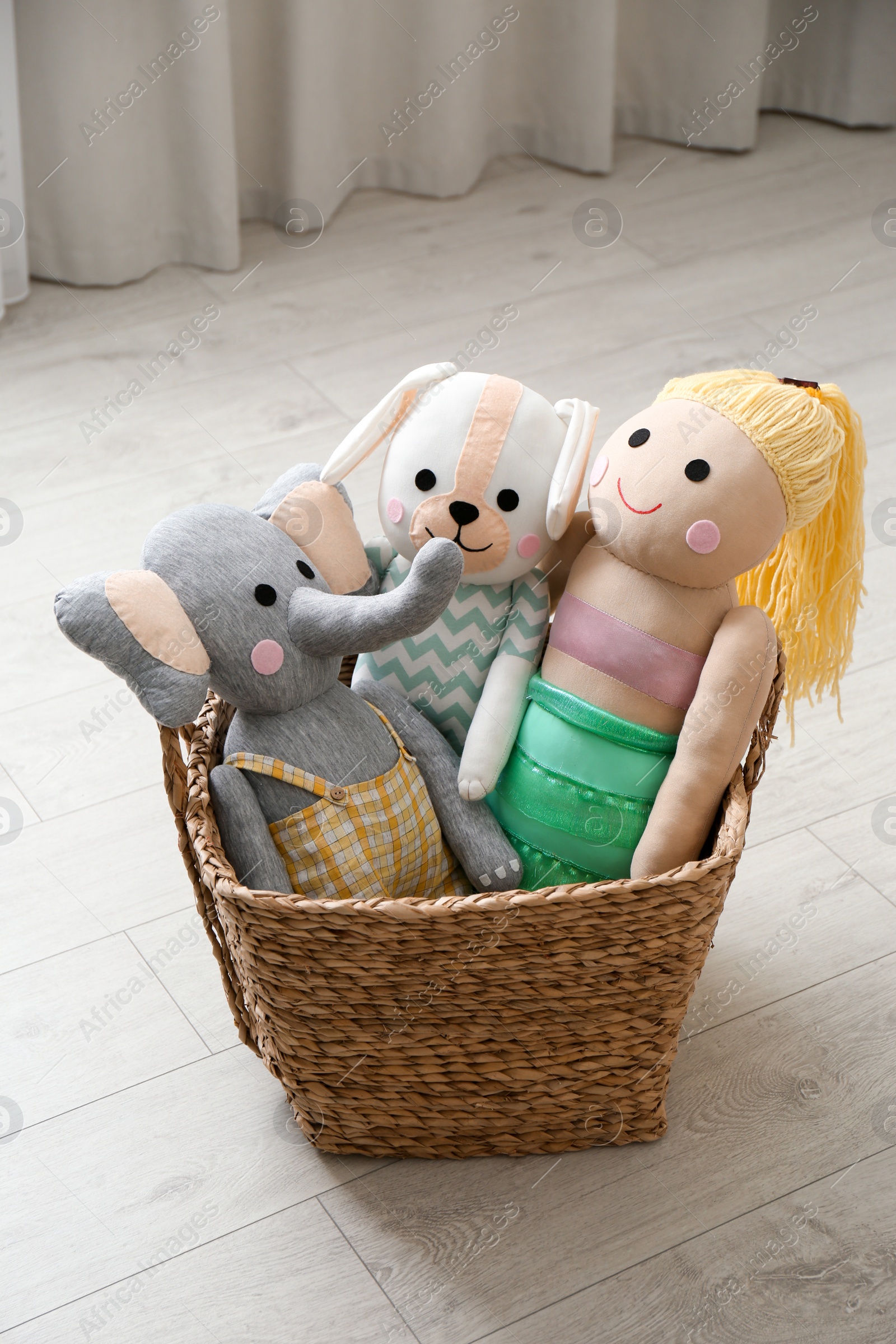 Photo of Funny toy elephant, dog and doll in basket on floor. Decor for children's room interior