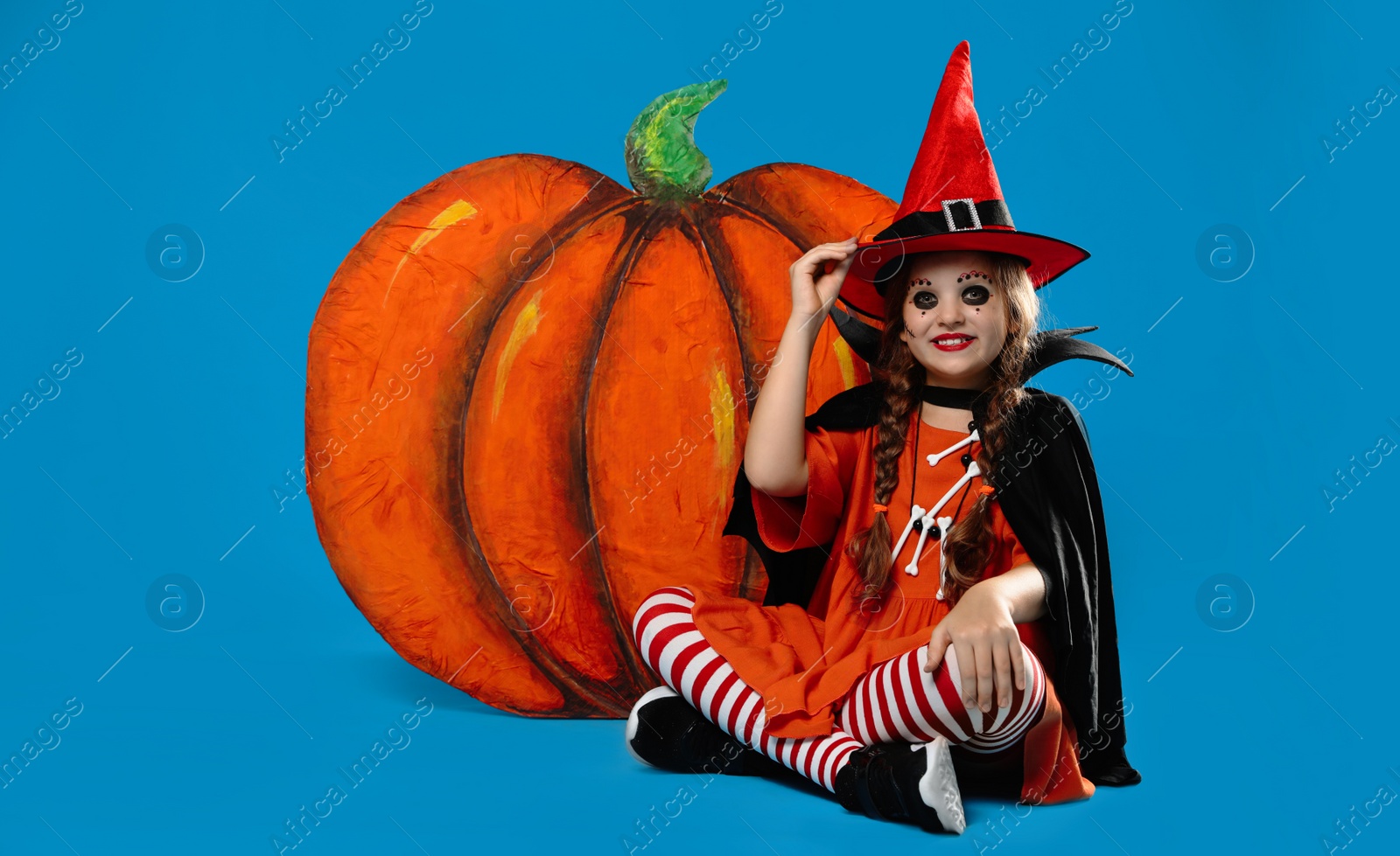 Photo of Cute little girl with decorative pumpkin wearing Halloween costume on light blue background