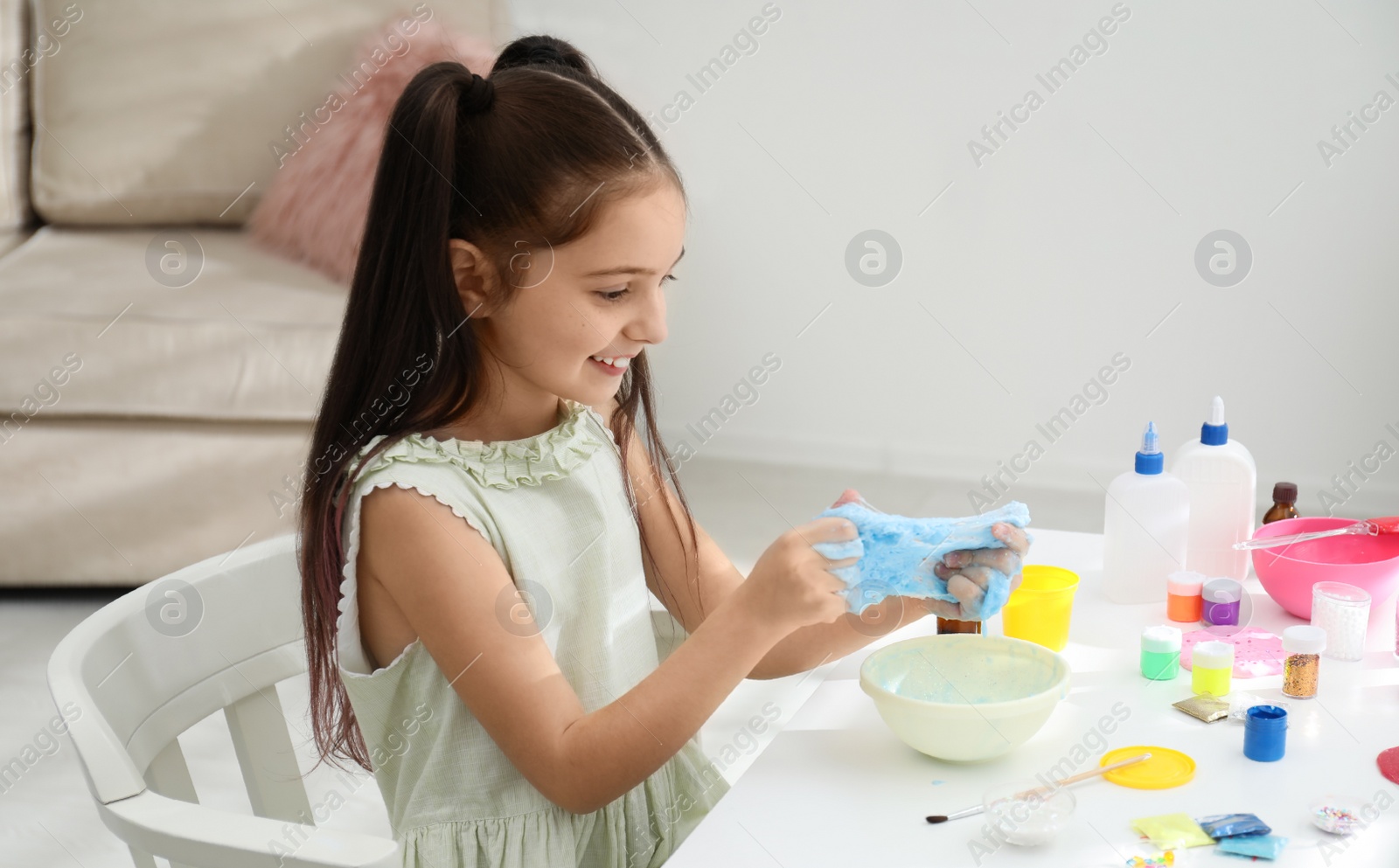 Photo of Cute little girl making DIY slime toy at table in room