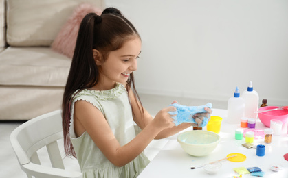 Cute little girl making DIY slime toy at table in room