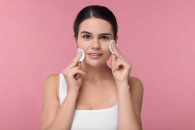 Photo of Young woman cleaning her face with cotton pads on pink background