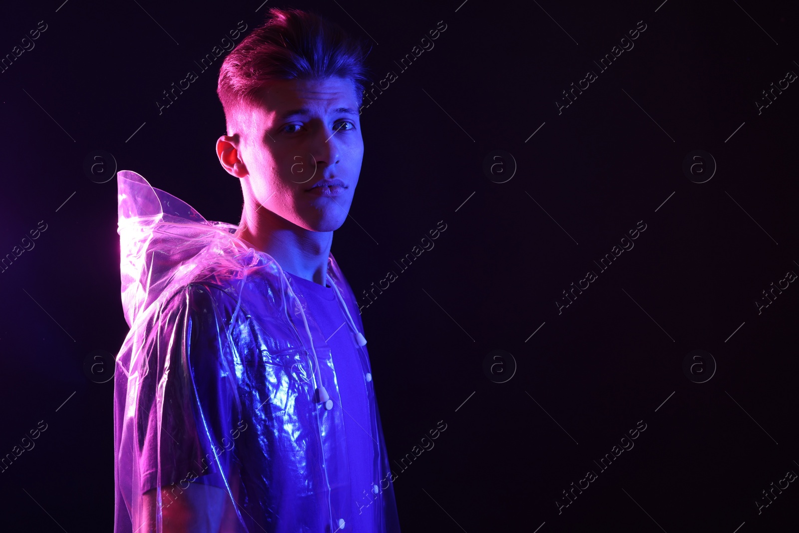 Photo of Young man wearing clear coat on dark background in neon lights. Space for text