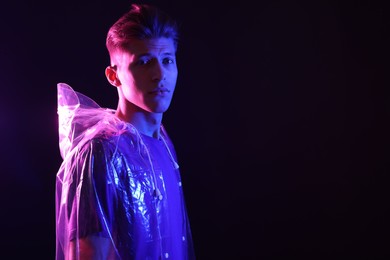 Photo of Young man wearing clear coat on dark background in neon lights. Space for text