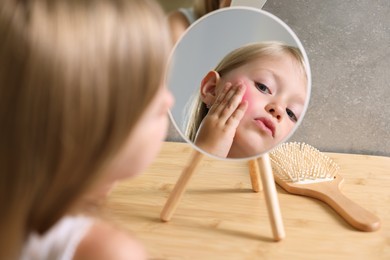 Suffering from allergy. Little girl looking at her face in mirror indoors