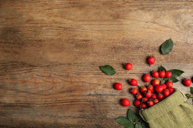 Ripe rose hip berries with green leaves on wooden table, flat lay. Space for text