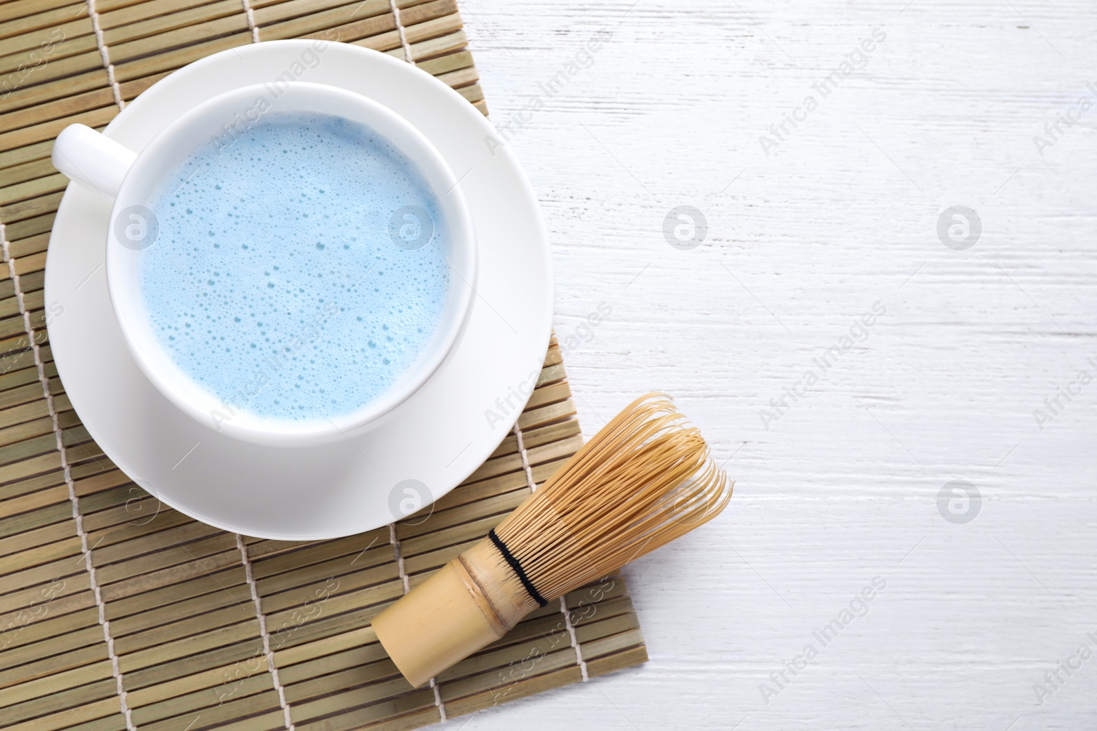 Image of Blue matcha latte, chasen and bamboo mat on white wooden table, flat lay