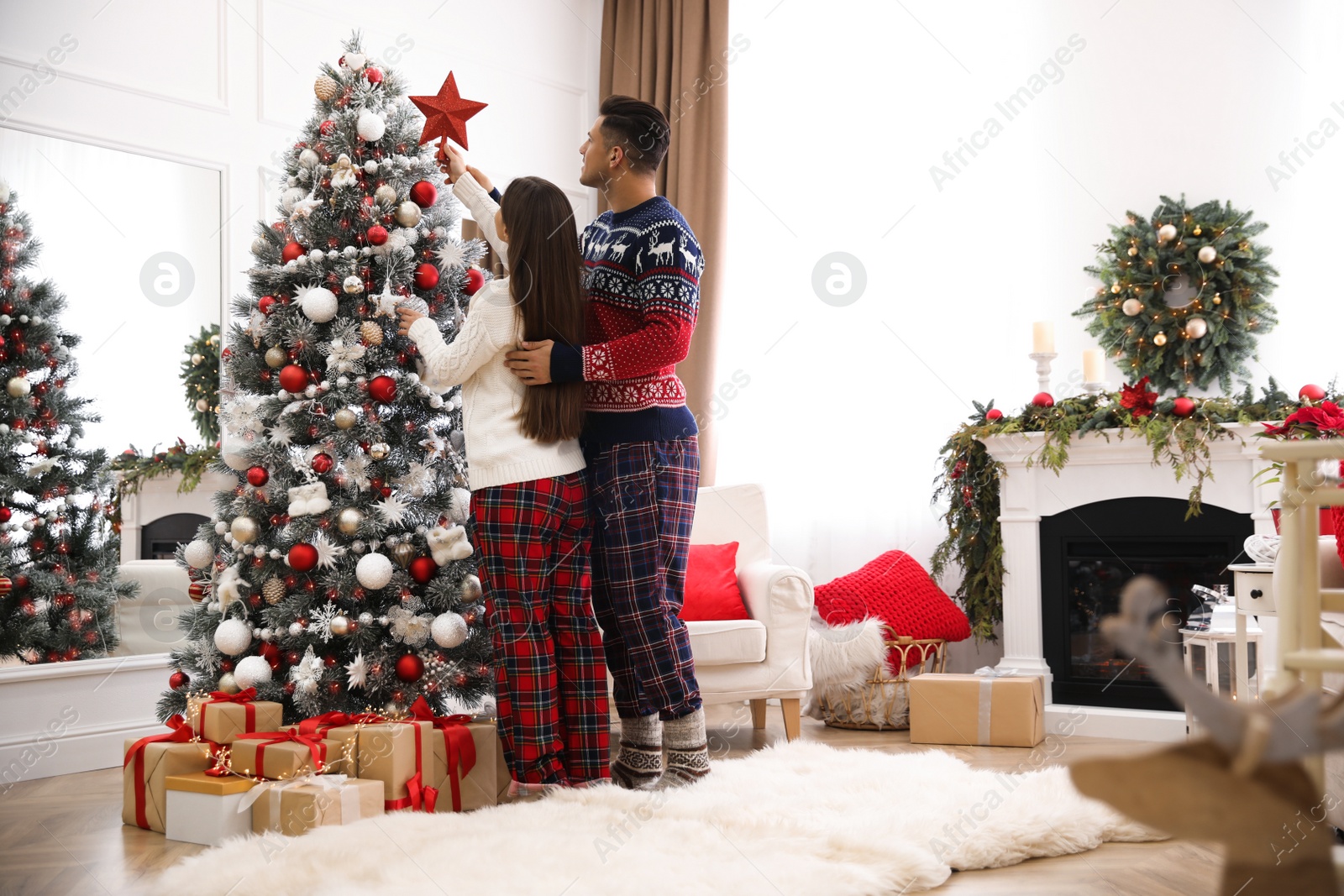 Photo of Couple decorating Christmas tree with star topper in room