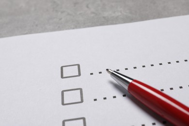 Paper sheet with checkboxes and pen on light grey table, closeup. Checklist