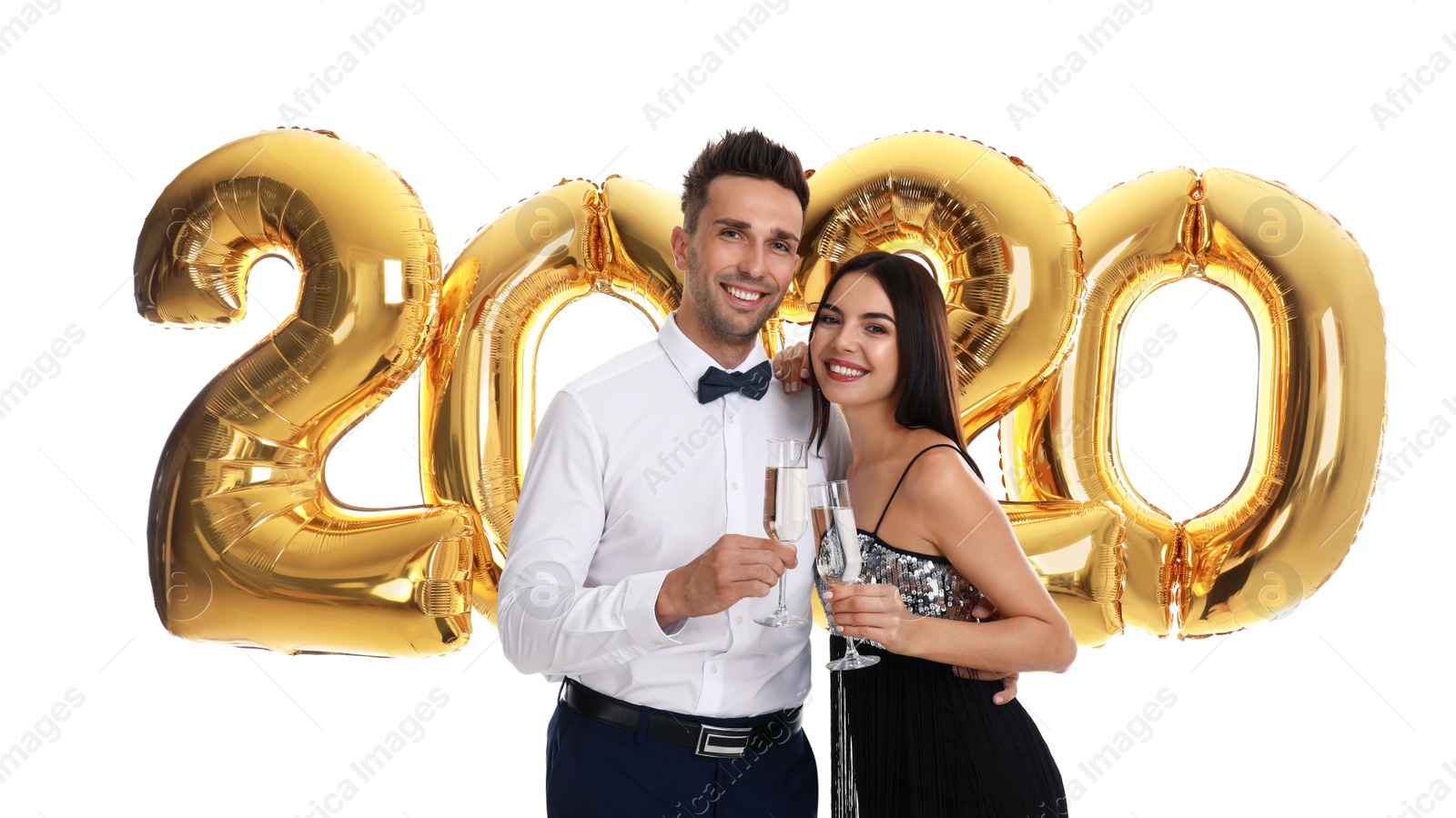 Photo of Happy young couple with glasses of champagne near golden 2020 balloons on white background. New Year celebration