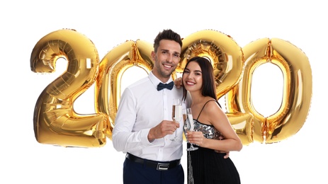 Happy young couple with glasses of champagne near golden 2020 balloons on white background. New Year celebration