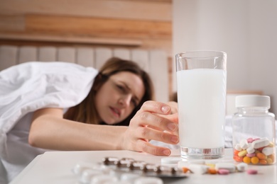 Photo of Woman taking medicine for hangover in bed at home, focus on hand with glass