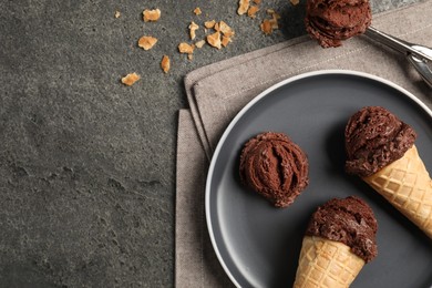 Chocolate ice cream scoops in wafer cones on gray textured table, flat lay. Space for text