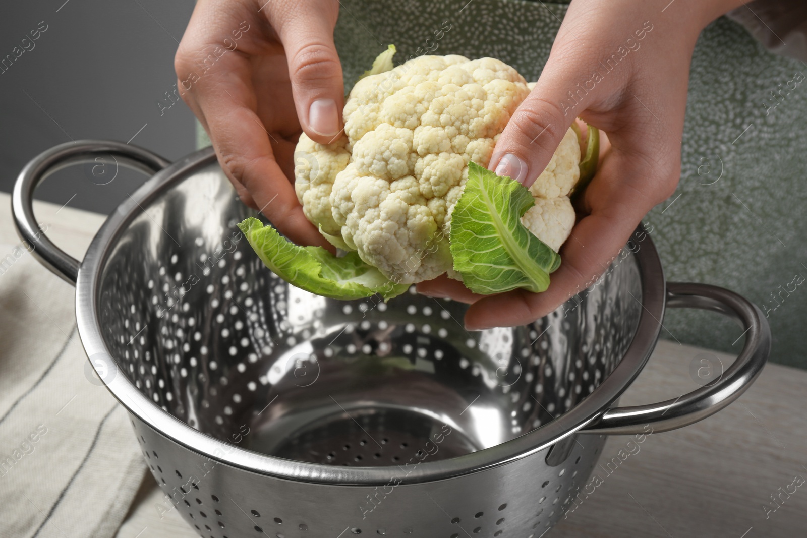 Photo of Woman holding fresh cauliflower cabbage above colander at wooden table, closeup