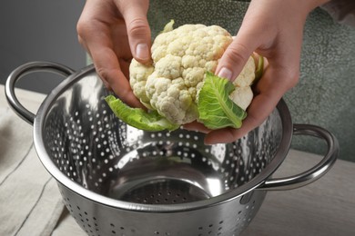 Photo of Woman holding fresh cauliflower cabbage above colander at wooden table, closeup