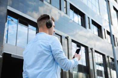Photo of Man in headphones using smartphone outdoors, low angle view. Space for text