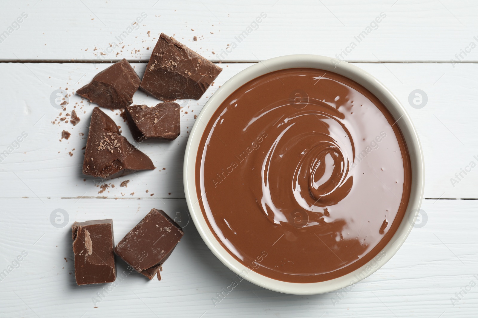 Photo of Tasty milk chocolate paste in bowl and pieces on white wooden table, flat lay