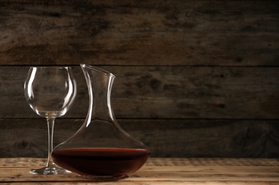 Photo of Elegant decanter with red wine and glass on wooden table