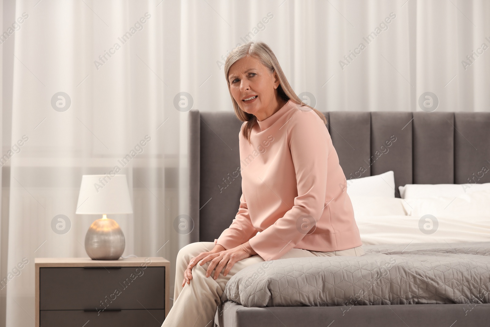 Photo of Mature woman suffering from knee pain on bed at home. Rheumatism symptom