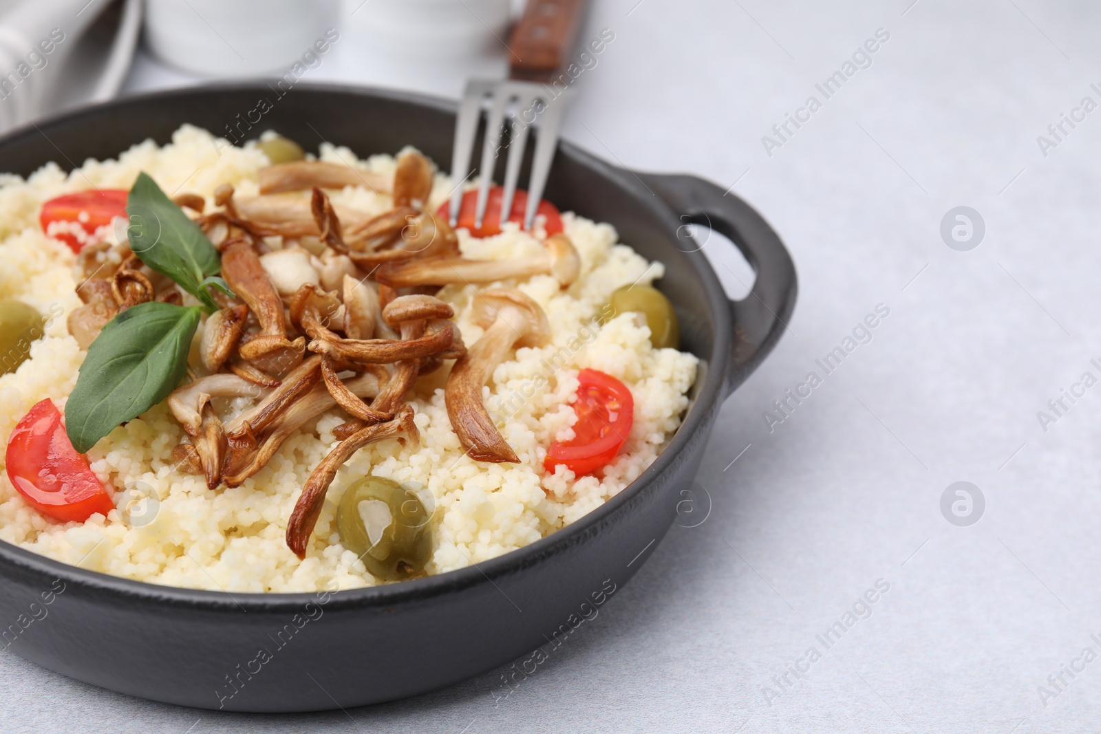 Photo of Tasty couscous with mushrooms, olives and tomatoes on grey table, closeup. Space for text