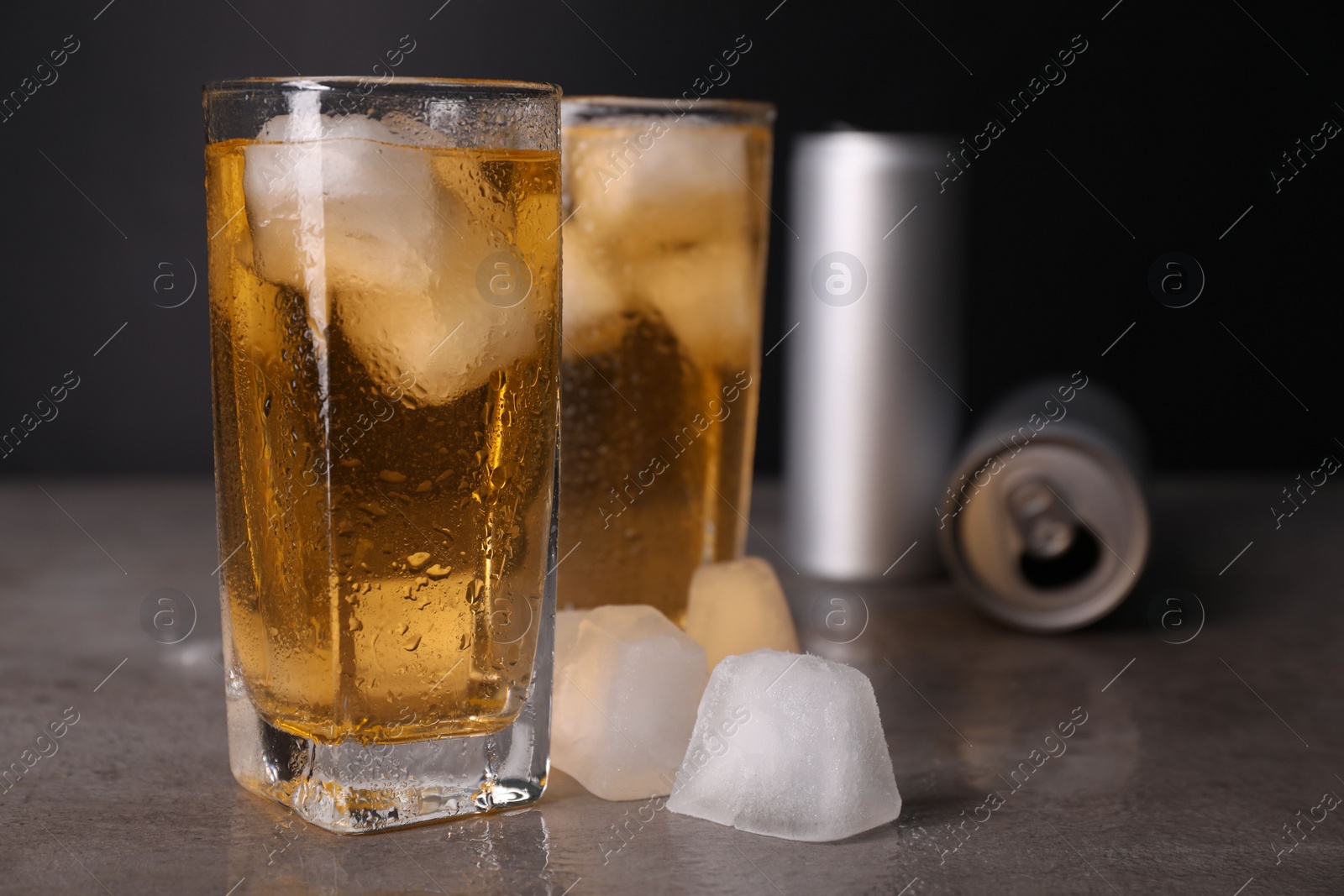 Photo of Tasty energy drink with ice cubes in glasses and aluminium cans on grey table, closeup