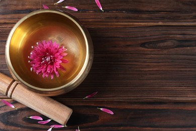 Photo of Tibetan singing bowl with water, beautiful flower, petals and mallet on wooden table, top view. Space for text