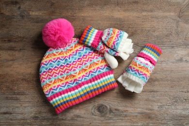 Warm knitted hat and mittens on wooden background, flat lay