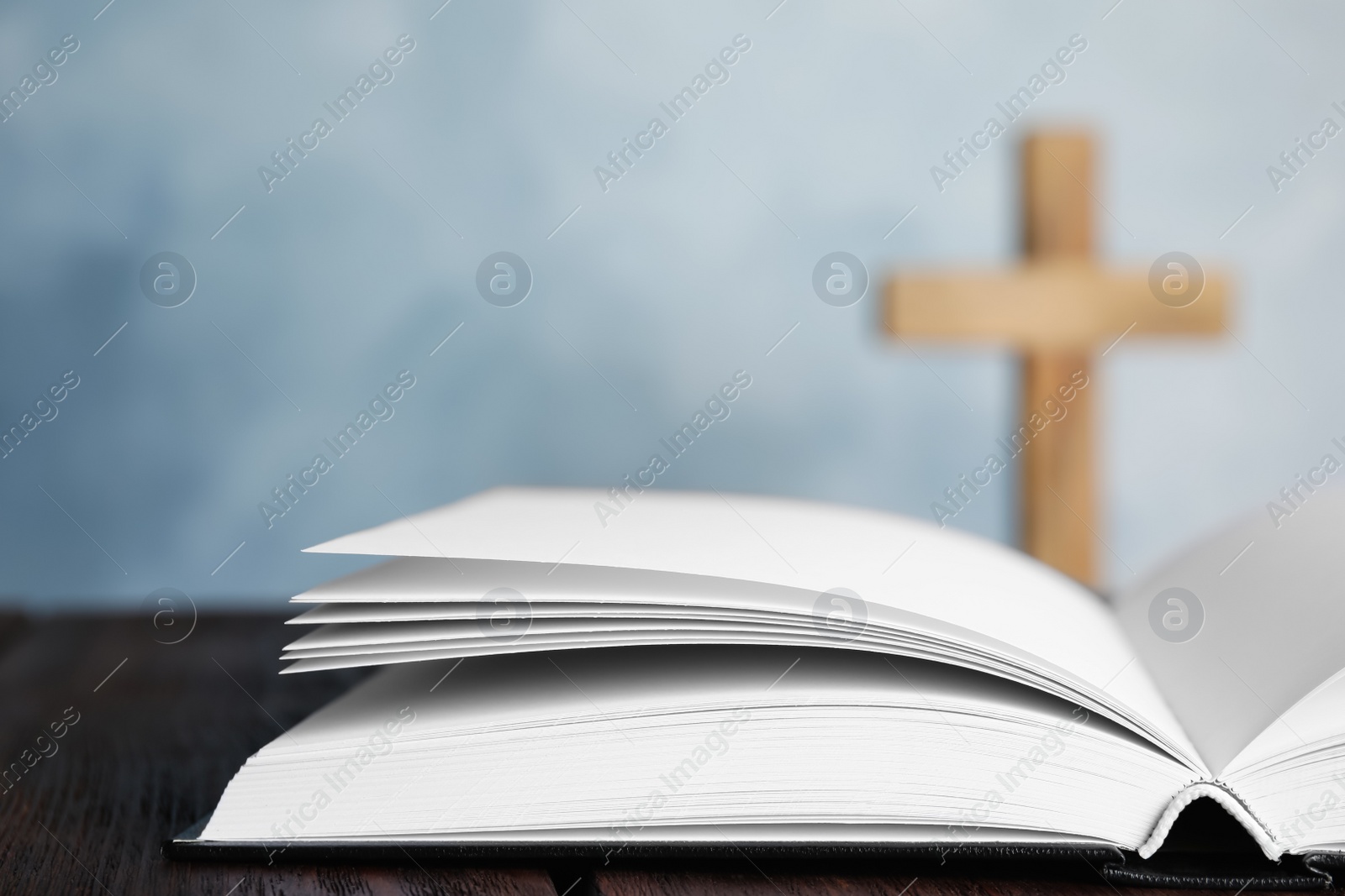 Photo of Open Bible on table and blurred cross on background, closeup. Christian religion