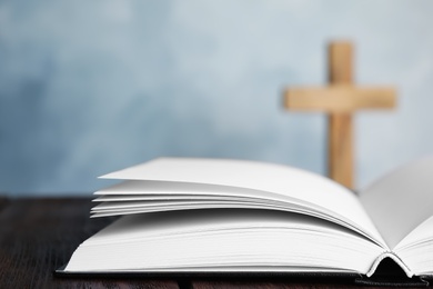 Photo of Open Bible on table and blurred cross on background, closeup. Christian religion