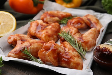 Photo of Raw marinated chicken wings and rosemary on wooden table, closeup