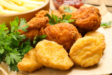 Photo of Tasty deep fried chicken pieces and nuggets on parchment, closeup