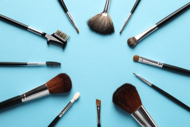 Frame of makeup brushes on light blue background, flat lay. Space for text