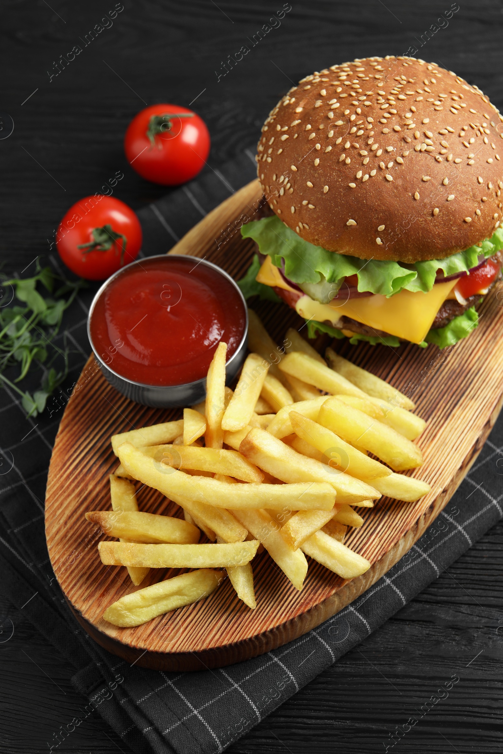 Photo of Delicious burger with beef patty, tomato sauce and french fries on black wooden table, above view